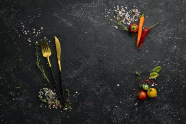 Sebze ve baharatlı siyah taş bir masanın üzerindeki çatal bıçak takımı. Yemek arkaplanı. Üst Manzara. Kırsal biçim.