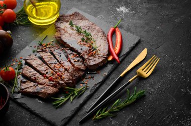 Baharatlı sulu dana biftek, kekik ve biberiye. Üst Manzara. Siyah taş kesme masasının üstünde düz bir görünüm vardı..