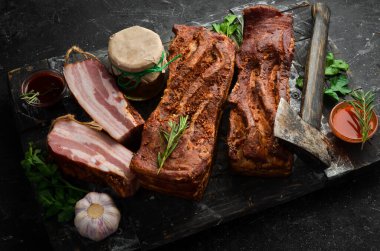 Baharatlı füme domuz pastırması. Siyah bir arka planda tütsülenmiş et parçası. Üst görünüm.