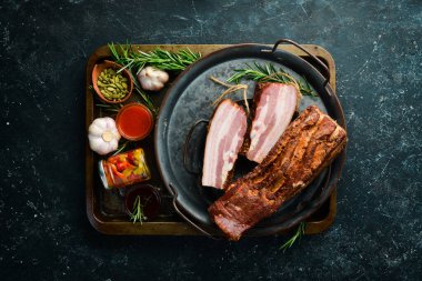 Baharatlı füme domuz pastırması. Siyah bir arka planda tütsülenmiş et parçası. Üst görünüm.