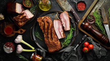 Baharatlı füme domuz pastırması. Siyah bir arka planda tütsülenmiş et parçası. Üst görünüm.