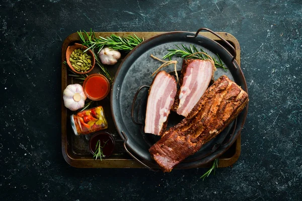 Baharatlı füme domuz pastırması. Siyah bir arka planda tütsülenmiş et parçası. Üst görünüm.