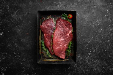 - Et. Biberiye ve baharatlı çiğ dana biftek. Siyah taştan bir arka planda. Üst görünüm.