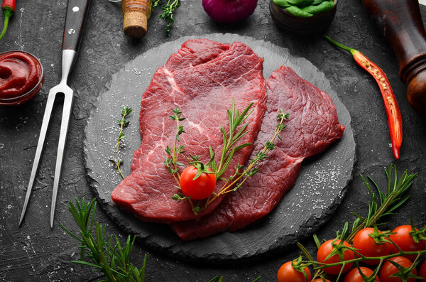 Meat. Raw veal steak with rosemary and spices. On a black stone background. Top view.