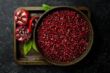 Tabakta olgun nar tohumları var. Taze nar meyvesi. Siyah taştan bir arkaplanda Üst görünümde.