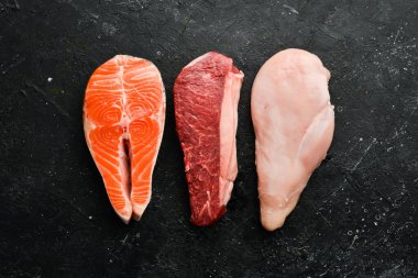 Çiğ yemek, somonlu biftek, dana eti, sığır eti ve tavuk, koyu taşlı arka planda. Üst Manzara. Organik yiyecekler.