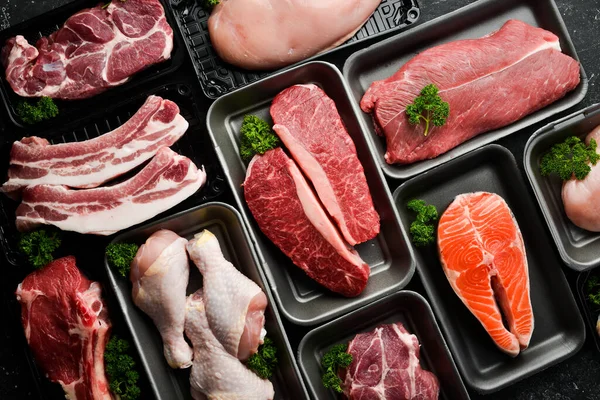 Set of fresh raw meat and fish in plastic boxes: veal, salmon steak, chicken, pork. Banner for the supermarket. On a dark background. Organic food.