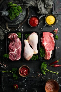 Taze çiğ et: dana eti, tavuk, domuz eti. Siyah taştan bir arka planda. Organik yiyecekler.