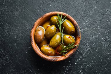 Marinated olives in a wooden bowl on a stone background. Free space for text.