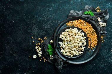 Prepared popcorn in frying pan, corn seeds in bowl and corncobs on kitchen table. Top view.