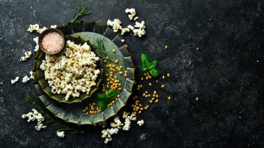 Prepared popcorn in frying pan, corn seeds in bowl and corncobs on kitchen table. Top view.