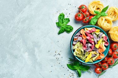 Gri taşlı arka planda bir kasede renkli kuru makarna. Yiyecekler. Üst Manzara. Metin için boş alan.