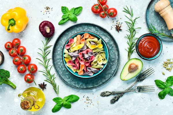 Gri taşlı arka planda bir kasede renkli kuru makarna. Yiyecekler. Üst Manzara. Metin için boş alan.