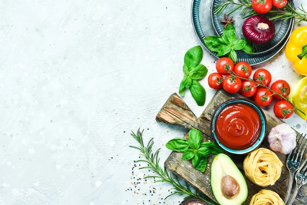 Preparation of pasta. Dry pasta and ingredients: tomatoes, basil, pepper and rosemary, on a gray stone background. Dry pasta. Top view. Free space for text.