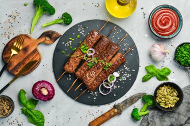 Siyah tabakta baharatlı şiş ızgara Lula kebabı. Betondan eski bir masanın üzerinde. Üst görünüm.