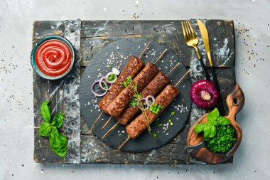 Siyah tabakta baharatlı şiş ızgara Lula kebabı. Betondan eski bir masanın üzerinde. Üst görünüm.