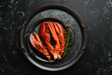 Metal bir tabakta baharatlı ve otlu ıstakoz pençeleri. Siyah taştan bir arka planda.