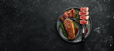 Izgara mermer biftekler çatalda çizgili. Siyah taştan bir arka planda.