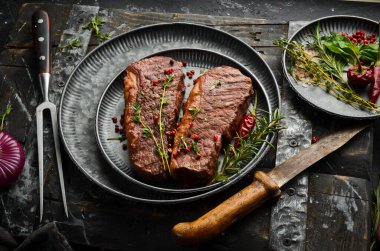 Izgara ribeye sığır eti biftek, otlar ve baharatlar karanlık bir masada. Üst te. Metniniz için boş alan.