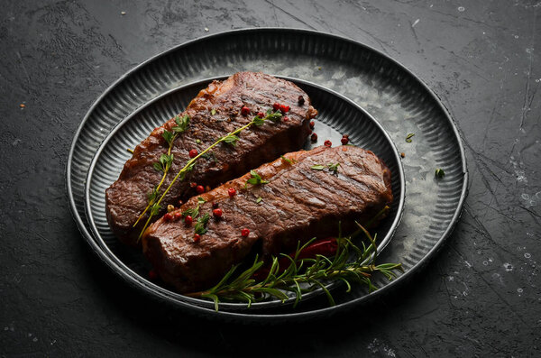Grilled ribeye beef steak, herbs and spices on a dark table. Top view. Free space for your text.