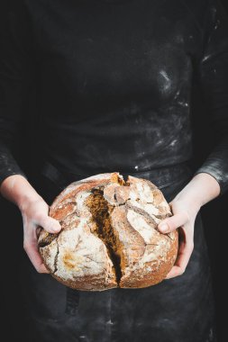 Undan yapılmış siyah ekmeği tutan kadın elleri. Siyah aşçılık arka planı.