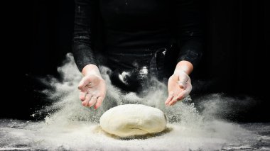 Kadın eli ekmek pişirmek için bir parça hamur tutuyor. Siyah aşçılık arka planı.