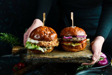 Eski bir tahtanın üzerinde bir şefin ellerinde lezzetli hamburgerler. Karanlık bir arka planda.