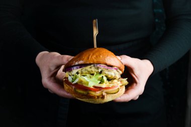Burger şefin elinde. Fast food konsepti. Karanlık bir arka planda.