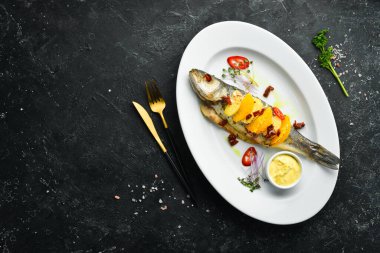 Beyaz tabakta portakal ve sebzelerle pişirilmiş levrek. Üst Manzara. Kırsal biçim.