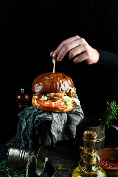 味道鲜美的烤汉堡包配鸡排 西红柿和洋葱 在手中 在黑色背景上 — 图库照片