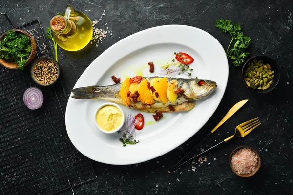 Beyaz tabakta portakal ve sebzelerle pişirilmiş levrek. Üst Manzara. Kırsal biçim.
