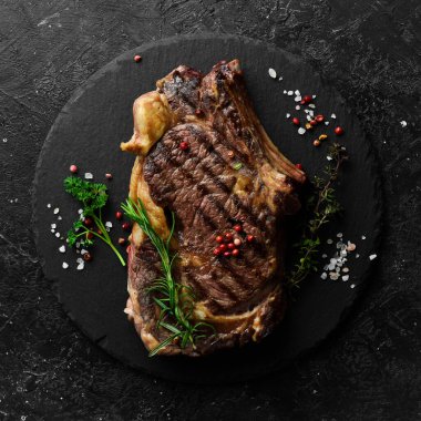 Izgarada pişmiş kemiğin üzerinde ızgara ızgara biftek. Barbekü. Siyah taştan bir arka planda.