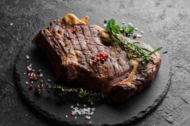 Izgarada pişmiş kemiğin üzerinde ızgara ızgara biftek. Barbekü. Siyah taştan bir arka planda.