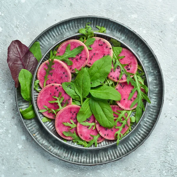 Sebze diyet salatası: ıspanak, karpuz turpu, siyah susam ve zeytinyağı. Vejetaryen yemeği. Üst Manzara. Taş bir arka planda.