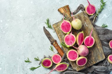 Mutfak tahtasında dilimlenmiş turp karpuzu. Beslenme amaçlı sebzeler. Gri taştan bir arka planda.