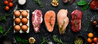 Keto diyet konsepti. Sıfır karbonhidrat ve düşük karbonhidrat diyeti için ham malzemeler. Pirzola, somon bifteği, domuz eti, yumurta. Üst Manzara. Siyah taştan bir arka planda.