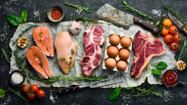 Keto diyet konsepti. Sıfır karbonhidrat ve düşük karbonhidrat diyeti için ham malzemeler. Pirzola, somon bifteği, domuz eti, yumurta. Üst Manzara. Siyah taştan bir arka planda.