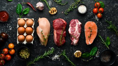 Keto diyet konsepti. Sıfır karbonhidrat ve düşük karbonhidrat diyeti için ham malzemeler. Pirzola, somon bifteği, domuz eti, yumurta. Üst Manzara. Siyah taştan bir arka planda.