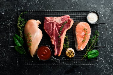 Farklı et setleri: somon bifteği, biftek ve tavuk göğsü. Siyah taştan bir arka planda.