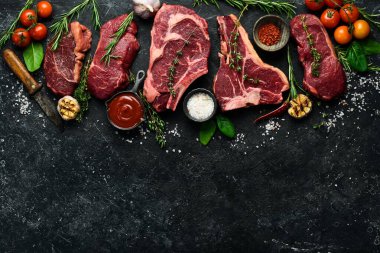 Çiğ biftek çeşitleri: t-bone, tomahawk, striploin, fileto, New York bifteği taştan arka planda ızgara yapmak için. Siyah taştan bir arka planda.