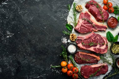 Çiğ biftek çeşitleri: t-bone, tomahawk, striploin, fileto, New York bifteği taştan arka planda ızgara yapmak için. Siyah taştan bir arka planda.