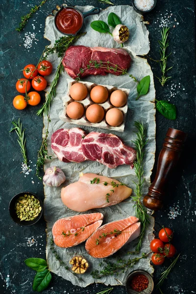 Various protein sources concept - rib eye, salmon steak, pork, egg. Top view. On a black stone background.