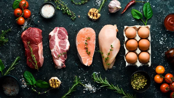 Various protein sources concept - rib eye, salmon steak, pork, egg. Top view. On a black stone background.