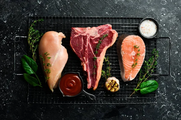 Farklı et setleri: somon bifteği, biftek ve tavuk göğsü. Siyah taştan bir arka planda.