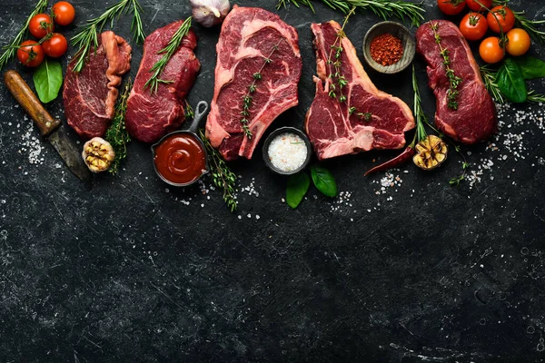 Çiğ biftek çeşitleri: t-bone, tomahawk, striploin, fileto, New York bifteği taştan arka planda ızgara yapmak için. Siyah taştan bir arka planda.