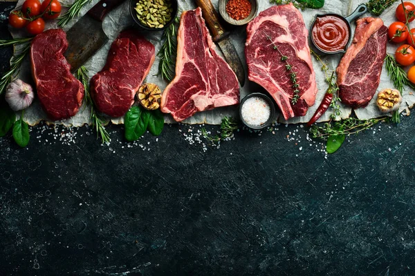 Çiğ biftek çeşitleri: t-bone, tomahawk, striploin, fileto, New York bifteği taştan arka planda ızgara yapmak için. Siyah taştan bir arka planda.