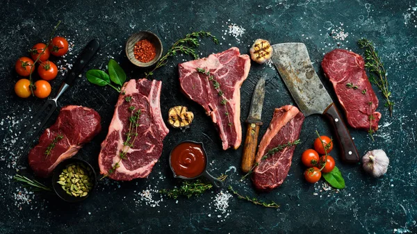 Çiğ biftek çeşitleri: t-bone, tomahawk, striploin, fileto, New York bifteği taştan arka planda ızgara yapmak için. Siyah taştan bir arka planda.