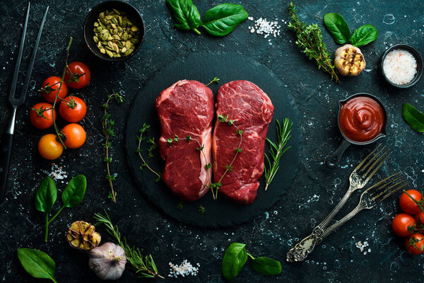 Two Raw striploin steak (New York) of beef on a board. Top view. On a black stone background.