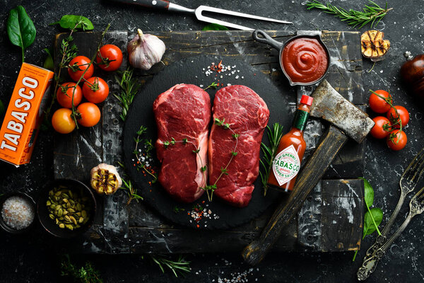UKRAINE, LVIV - February 10, 2022: A bottle of Tabasco sauce with Raw striploin steak. Top view. On a black stone background.