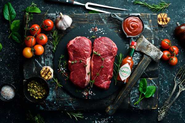 UKRAINE, LVIV - February 10, 2022: A bottle of Tabasco sauce with Raw striploin steak. Top view. On a black stone background.